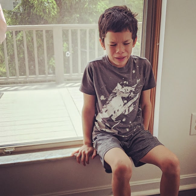 Boy crying on window ledge after not getting his way. 