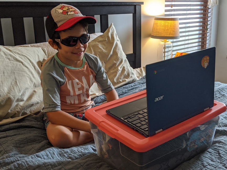 Kindergartner having school from home looks at laptop while wearing sunglasses, as part of our COVID-19 family routine. 