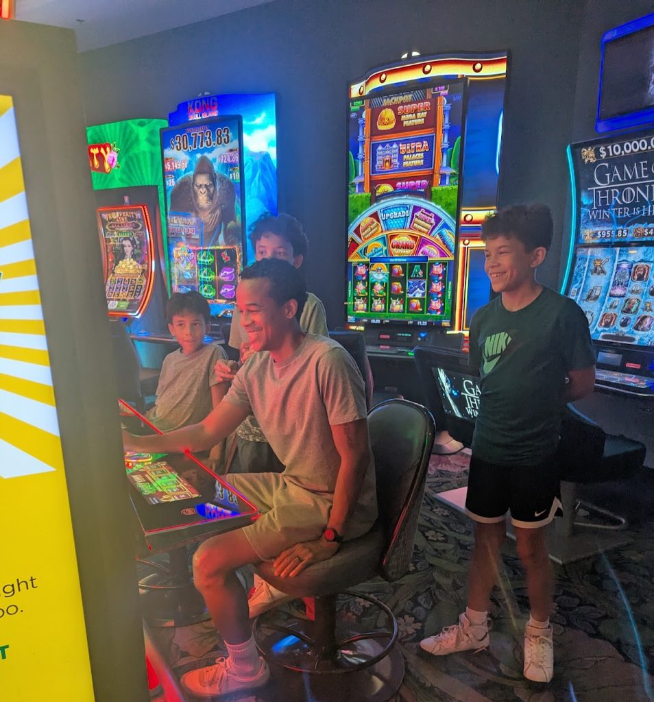Father playing the slots at Park MGM as kids look on. 